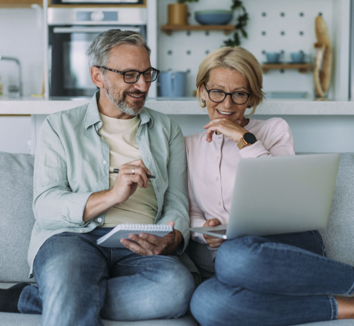 Couple sitting on the couch reviewing their finances on a laptop