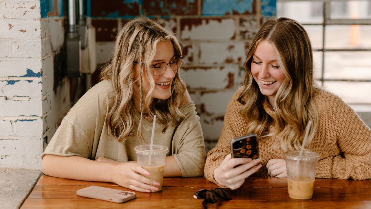 Friends enjoying a coffee date and laughing about something on their phone